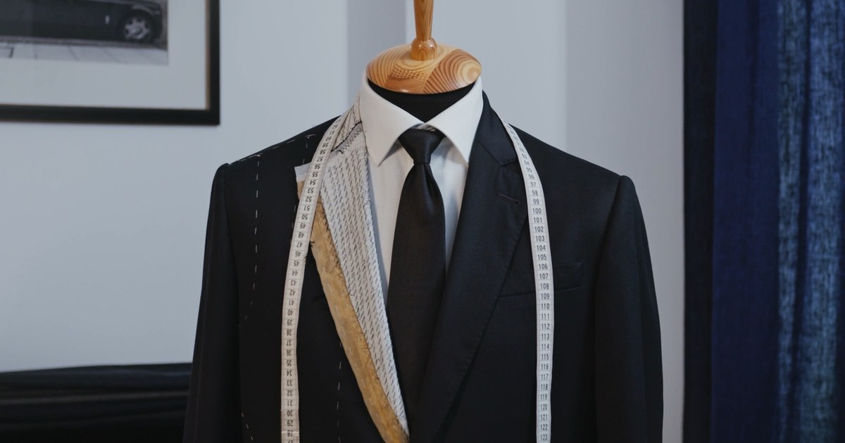 The Sumer demo &mdash; a bespoke tailor: six beats of hand tailoring built by the scroll, a tailor&rsquo;s tape unrolling beside them, the name landing on the basted lapel